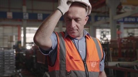 Close up, male engineer caucasian at an industrial factory takes off his hat to wipe away the sweat on his face.