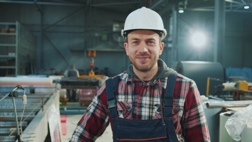 Handsome industry engineer man wears safety uniform and hard hat stand look at camera smiling feel happy in factory. Inspector in warehouse. Royalty-Free Stock Footage #1088878893