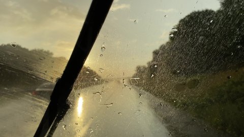 Pouring rain on the windshield of a car while driving on the highway facing the afternoon sun and giving the wipers a hard time  