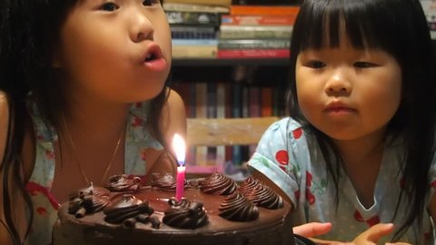 Beautiful asian toddler girls eating cake and blowing out candles
