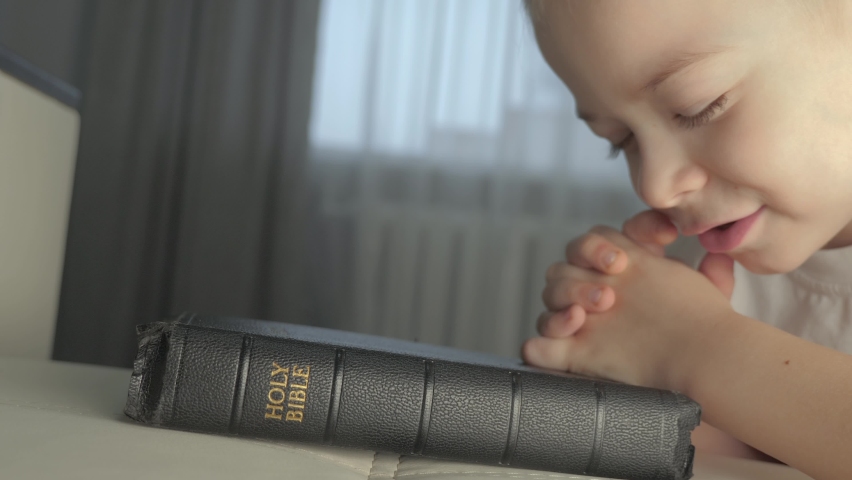 Little boy praying bible. lifestyle religion concept holy book bible. little boy prays at home in the evening by the bed on the bible | Shutterstock HD Video #1088884197