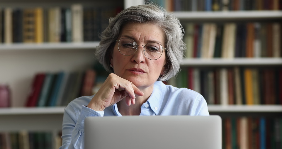 Close up smiling attractive older 50s businesslady in glasses working on laptop sit at desk in modern office look concentrated and motivated. Busy workday, workflow using modern tech, blogging concept Royalty-Free Stock Footage #1088885279