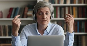 Older grey-haired woman sit at workplace looking at laptop, makes speech use video conference app, take part in videocall by business, communicating, provide help remotely, on-line counselling concept