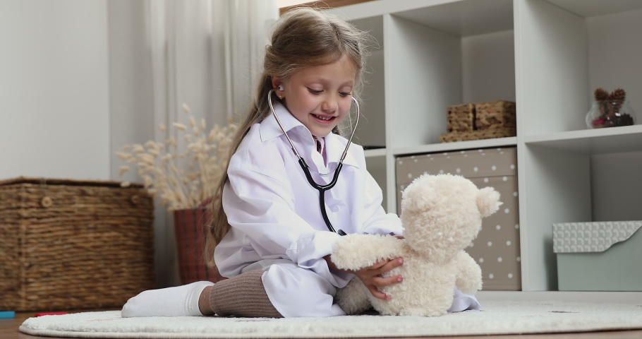 Cute little girl wear uniform use stethoscope listens heartbeat to stuffed toy bear, takes care, heal best plush friend, play clinic. Health-care, pediatrician, future profession and vocation concept Royalty-Free Stock Footage #1088885401