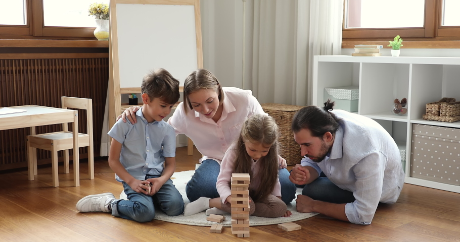 Young couple and siblings play game sit on floor in playroom. Little boy and girl spend weekend leisure with loving parents enjoy wooden tumbling tower boardgame. Family fun, kids development concept Royalty-Free Stock Footage #1088885415