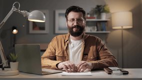 Man looking at camera and speaks. Bearded teacher with glasses in home office is talking on video call. Remote online salesperson makes presentation from apartment