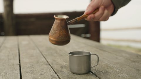 Coffee is poured into a metal mug made of copper cezve. The concept of outdoor recreation.