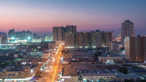 Cityscape with towers in Ajman from rooftop day to night timelapse with towers and traffic on a big road. Aerial view of illuminated buildings after sunset in the United Arab Emirates.