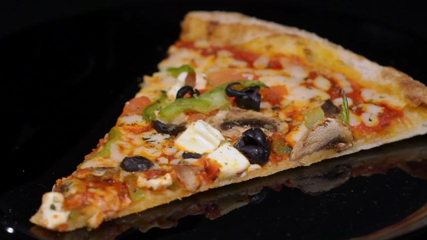 Piece slice of pizza with vegetables and cheese. Olives, pepper and tomato. Food on plate turning on black isolated background. Showcase in restaurant pizzeria.
