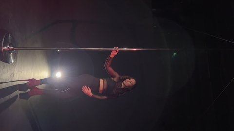 Vertical video. Pole dance. Young beautiful caucasian brunette woman dancer in studio at black background. Girl dancing striptease. Sexy female in shoes on high heels strips, pants and crop top.
