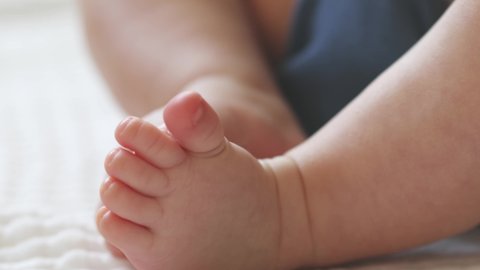 close-up bare feet and toes of infant baby legs in white sheet. newborn tiny fingers feet moving. caucasian little baby foot macro view. barefoot child legs 