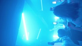 Vertical video. A crowd of people dancing on the dance floor of a nightclub under the light of colored spotlights. People are shooting videos on their smartphones. Night club