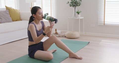 Young asia active teen slim fit girl finish morning routine yoga at home gym check plan result on phone drink diet protein shake water bottle post on IG reel tiktok show share online social media app.
