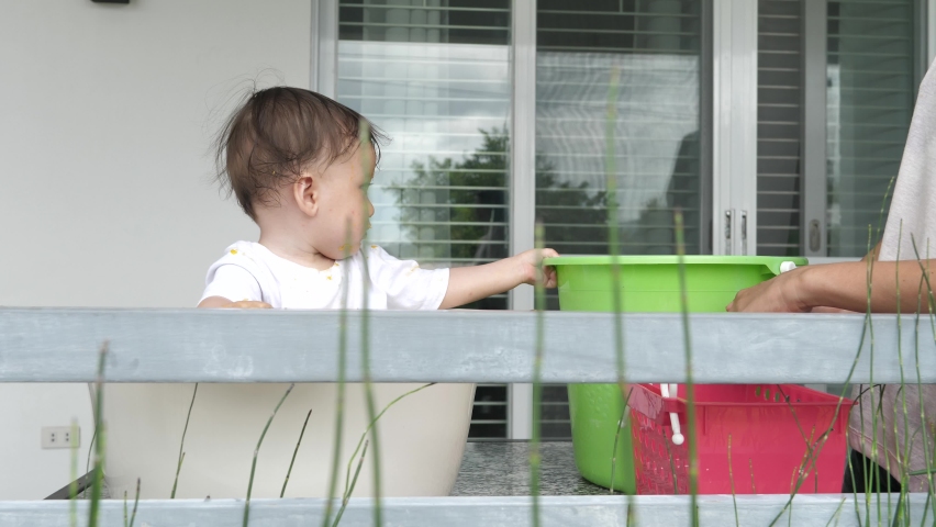 Mom helps the baby to get to know this world better. A cute baby sits in a basin and tries to get on his feet, his mother helps him and takes care of the baby. Baby hygiene is the key to good health.