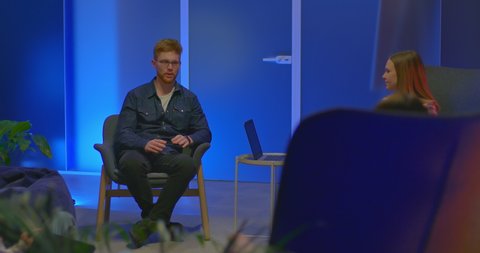 Red-haired guy sits in a chair and talks with colleagues, meeting partners. Guy with glasses talks about a new business project, a modern coworking office. 4k, ProRes