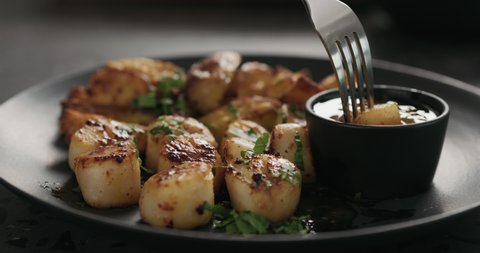 Slow motion eat roasted scallops with baked potatoes on black plate