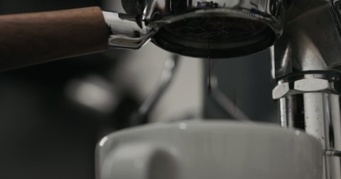 Slow motion low angle shot of extraction espresso with bottomless portafilter into white cup