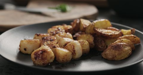 Slow motion arrange baked potato wedges to roasted scallops on black plate