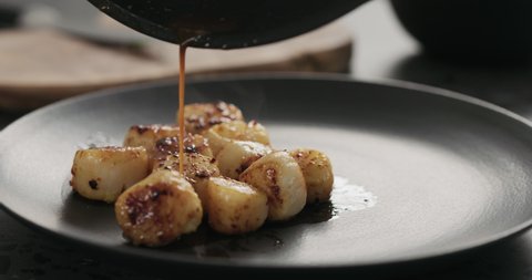 Slow motion drizzle roasted scallops with juice from frying in black plate