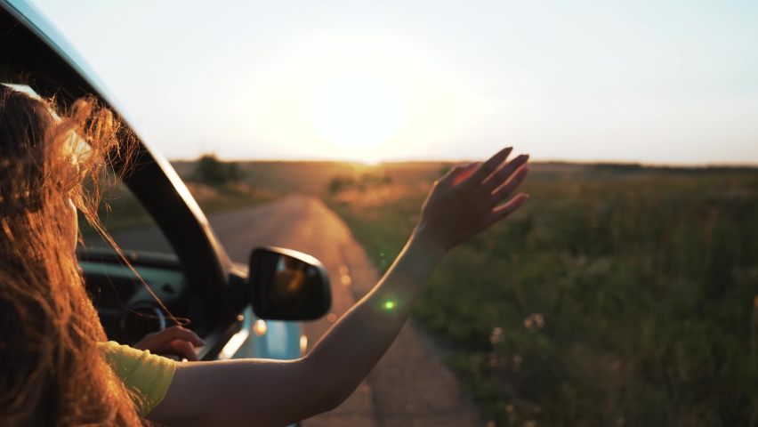 Happy girl in car window. Hair in wind. Girl travels by car. Hand in sun. Windy breeze from car window. Happy girl smiling from car window. Windy breeze in your hair. Hand in the rays of the sun | Shutterstock HD Video #1088898995