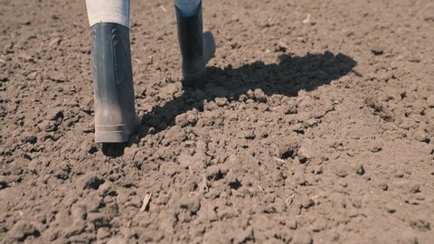 agriculture concept. plowed field land. farmer walks across field land rubber boots. work nature eco. farmland crop planting time. gardener works garden. legs boots close-up. farming concept
