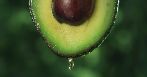 Cinematic macro shot of half raw fresh organic tropical green avocado fruit with falling oil drop isolated on green background.