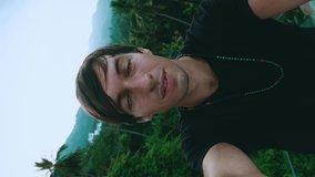 Vertical video portrait of smiling young man tourist making a selfie or video call on green jungle forest background. Young male travels tropical country doing a video chat.