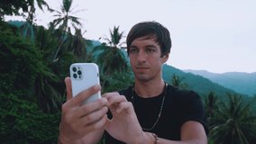 Young man traveler making video call on smartphone outdoors on beautiful jungle background