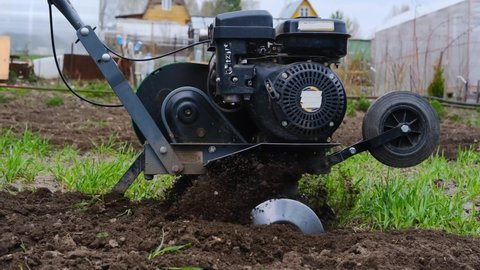 Elderly man plows the soil with a cultivator or tillerblock. 
