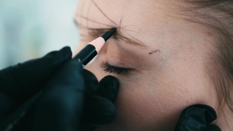 Cosmetologist drawing right shape of eyebrows for model during permanent makeup process