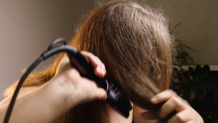 A woman combs her hair with a special electric straightening brush. The ceramic heated brush does not damage the hair. Close-up Royalty-Free Stock Footage #1088908851