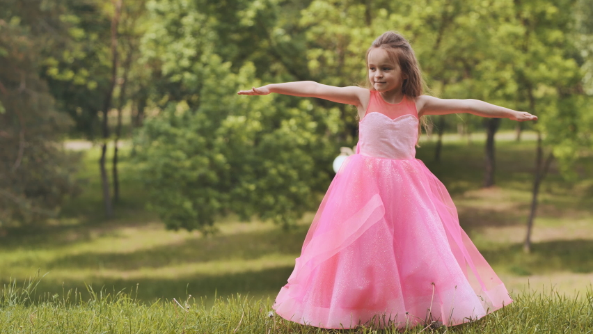 A girl in a pink princess dress is spinning in the park.