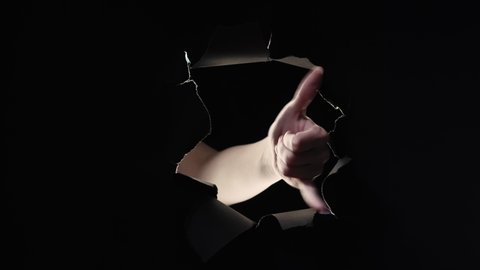 Call gesture. Shaka sign. Hang loose. Female hand showing ringing phone sign inside black breakthrough paper hole ripped wall isolated on dark night copy space background loop.