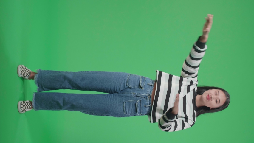 Full Body Of A Smiling Asian Woman Dabbing While Standing In Front Of Green Screen Background  
