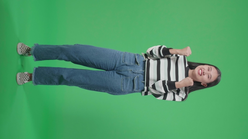 Full Body Of A Happy Asian Woman Celebrating While Standing In Front Of Green Screen Background
