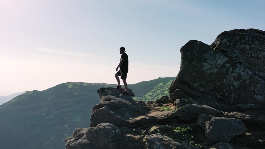 A tourist on top of the mountain raising his hands rejoices at the beautiful scenery