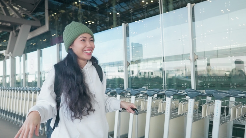 Attractive asian long curly hair woman pushing baggage trolley at airport street with happily waving hands to friend, customer waving hand, pick up service, female tourist travelling, greeting people Royalty-Free Stock Footage #1088917081