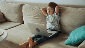 Child watching video and using laptop, sitting on sofa at home