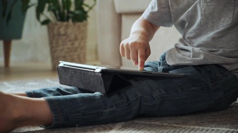 Child using tablet sitting on the floor at home, entertainment and playing online games