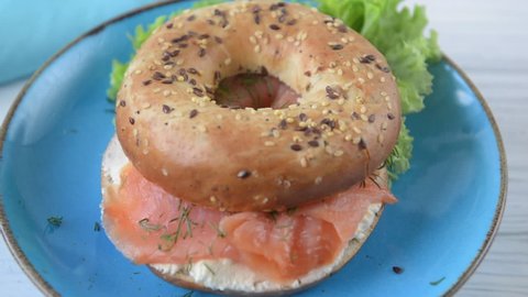 Multigrain bagel with cream cheese, salmon slices, dill and salad. Top bagel bun falling. Food drop. Slow Motion.