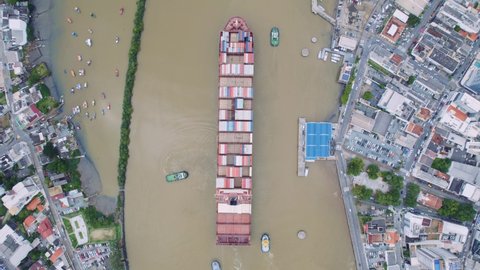 Aerial view of a large container freighter heads out to the sea assisted by tugs
