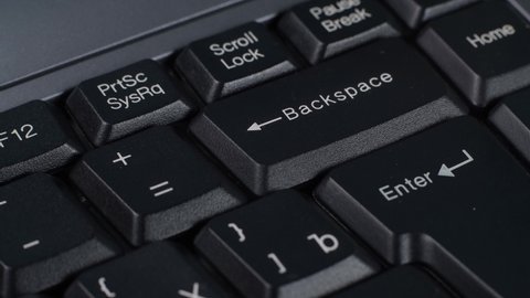 A man presses the Backspace and Enter key on a black computer keyboard, close-up.