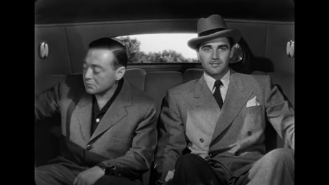 CIRCA 1946 - In this film noir, a gangster controls the speed of his car from the backseat, speeding them towards an oncoming train.