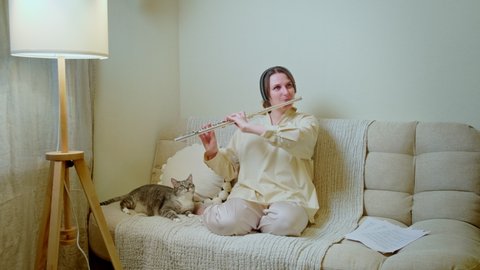 Happy woman with a flute is playing at home on the sofa in the living room