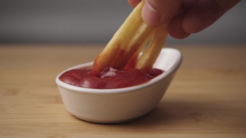 Mixing tomato ketchup sauce with french fries on a wooden background. Closeup view. Junk food concept