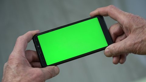 Elder person holding in wrinkled hands black phone with chroma key on horizontal screen