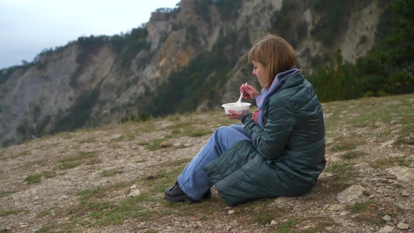 Woman tourist has lunch in the mountains. Girl enjoys eating outdoors