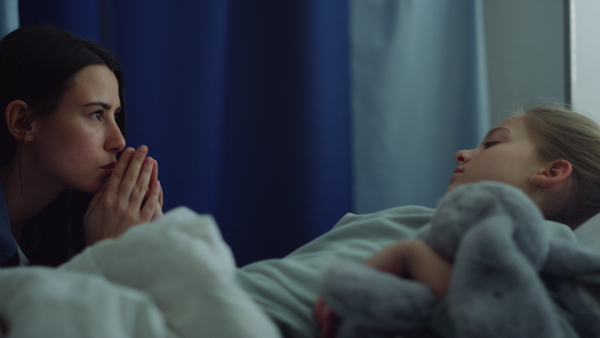 Upset woman visiting sick little girl in clinic. Child lying in hospital bed. Anxious young mother sitting holding seriously ill daughter hand in ward. Worried female desperately praying for recovery. Royalty-Free Stock Footage #1088927541