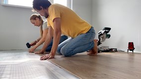 A family of woman and man install laminate on the floor in their apartment. DIY concept. Slowmotion video