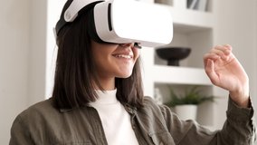 Beautiful young female playing game in vr glasses. Happy woman touch something using modern virtual reality glasses. Augmented Reality. Student playing using VR glasses on a sunny day. Home interior  - Powered by Shutterstock - Get 15% off with code: PIKWIZARD15